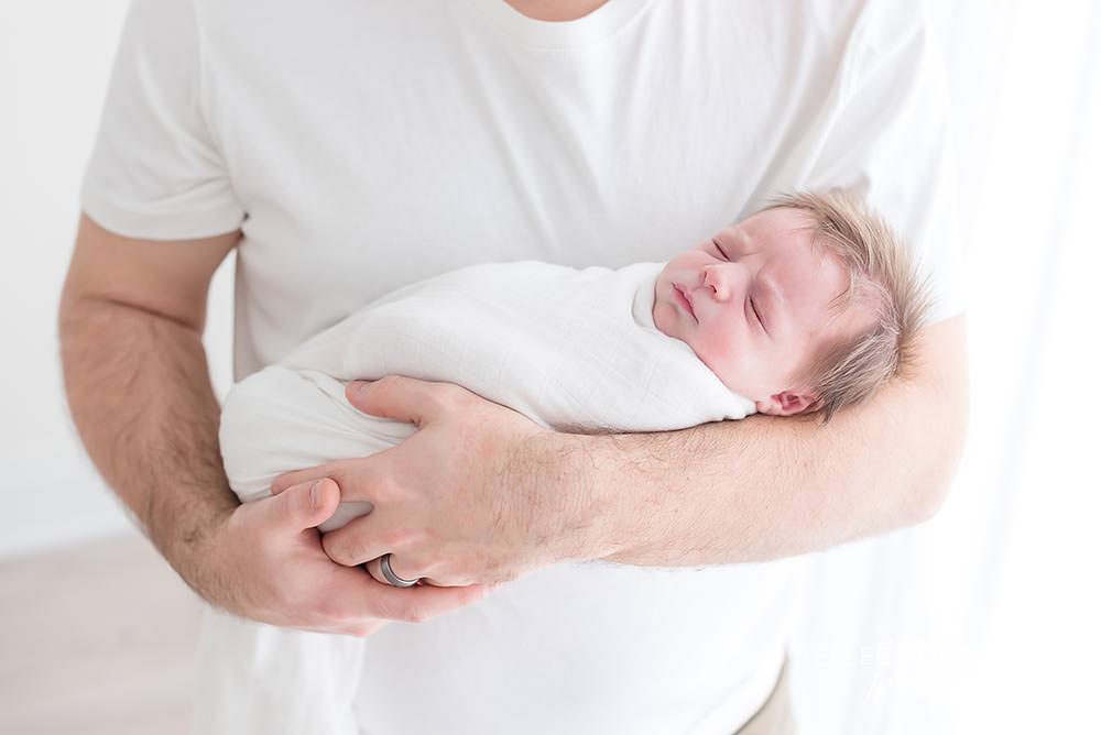 father holds his baby as it sleeps in natural light studio