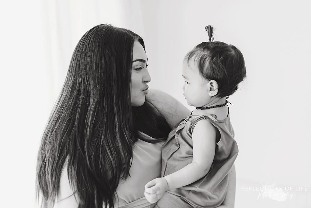 mama makes a kissy face to her daughter in black and white