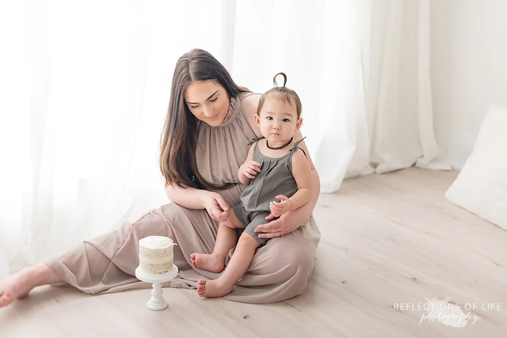 mama and baby sit beside the cake and baby looks at the camera