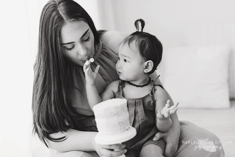 little girl feeds her mama icing off of the cake in black and white