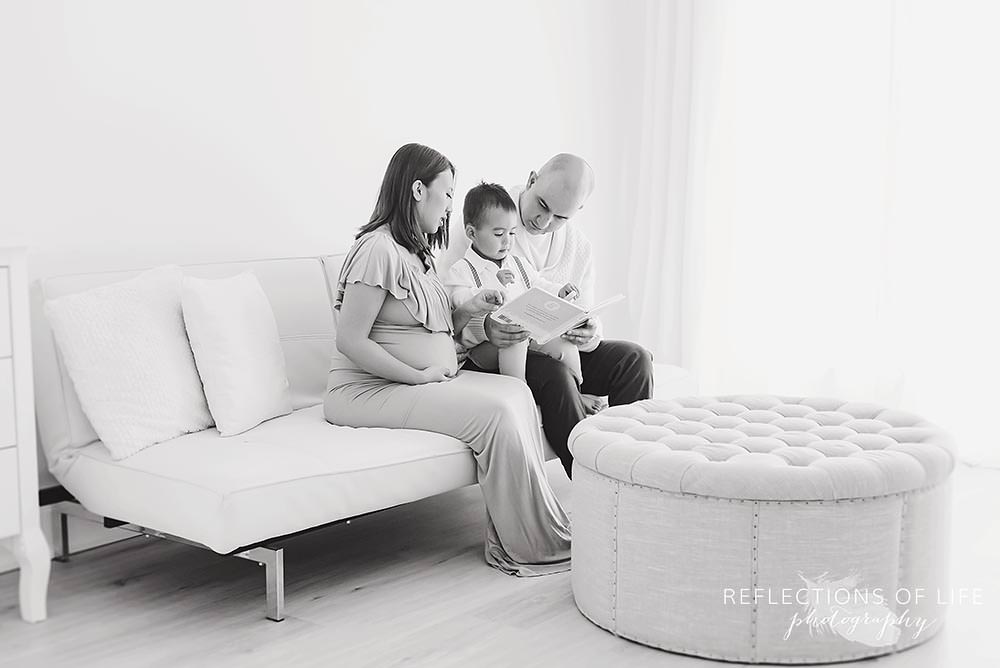 family of three sit on a couch in natural light studio in black and white