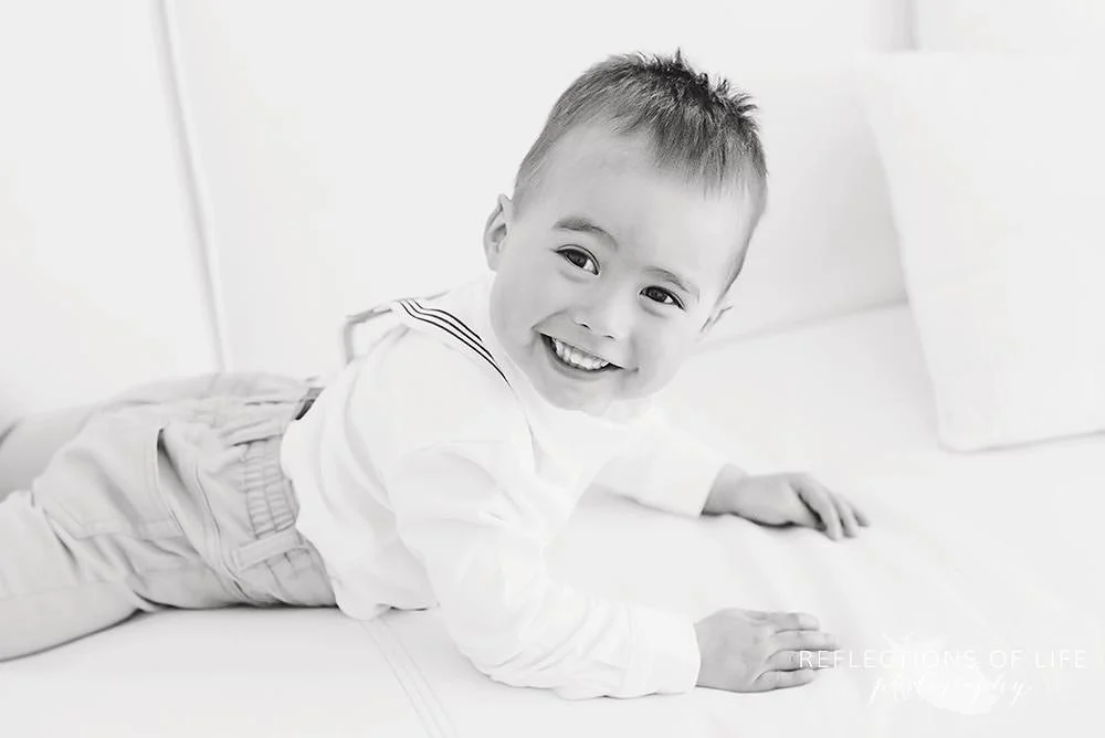 little boy looks back at his mama as he lays on the couch in black and white