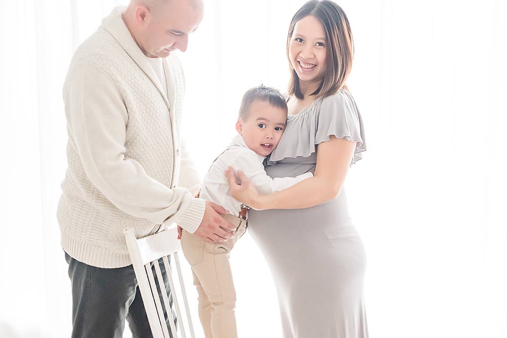 little boy stands on a chair so he can hug his mama while dad supports him