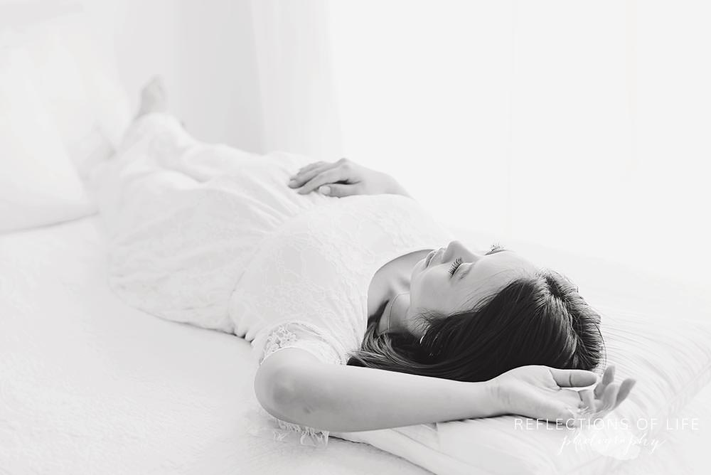 mama holds her belly as she lays on the bed in black and white