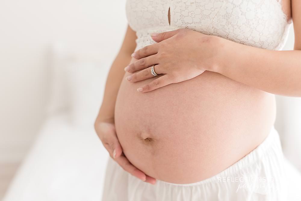 close up of mama holding her bump with her ring on her hand in natural light studio