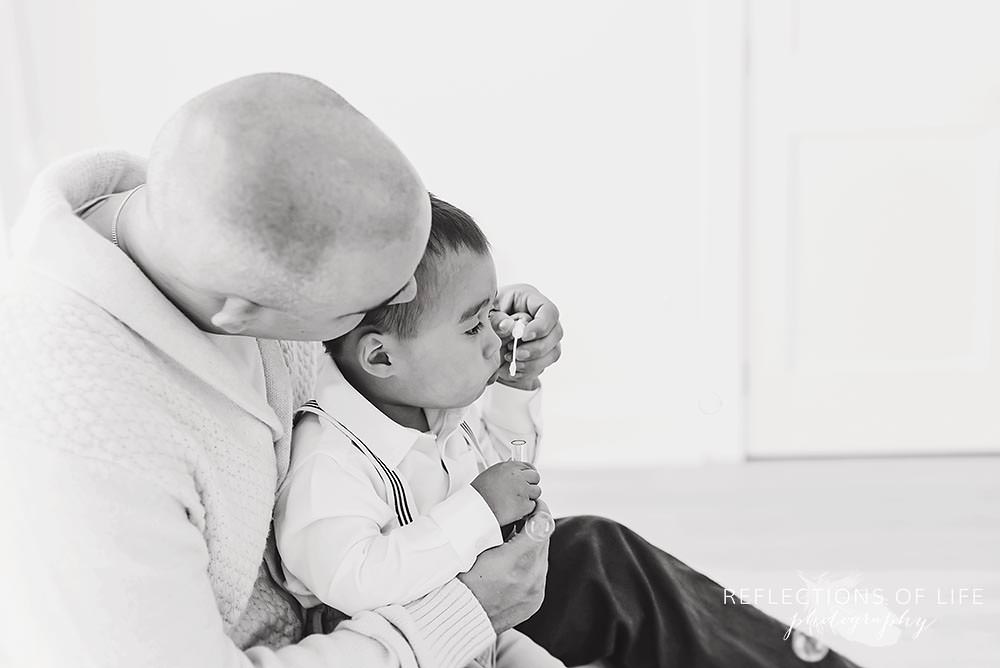 dad guides his son while he tries to blow a bubble in black and white