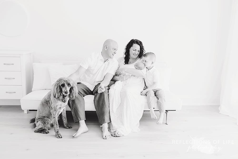family of four fits on a couch as parents smile at their son in black and white