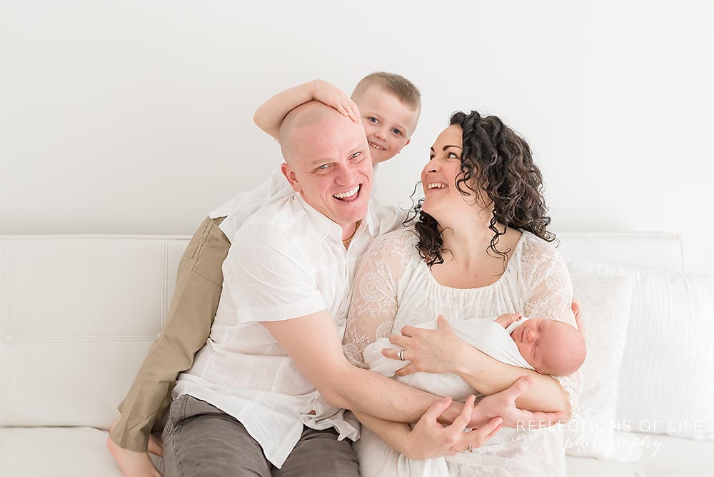young family gets silly as little boy pushes his dads head as they laugh
