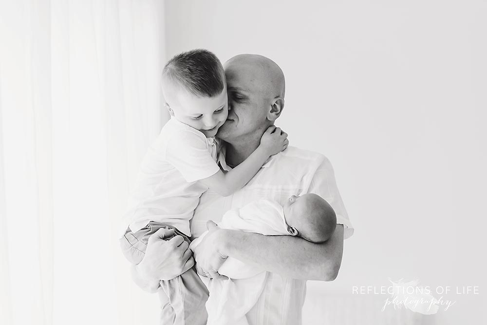 dad holds his two babies as he hugs them in black and white