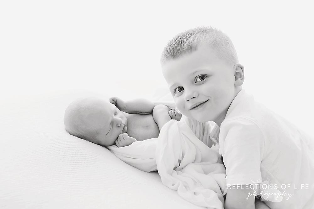 brother joins his new sibling and smiles in black and white