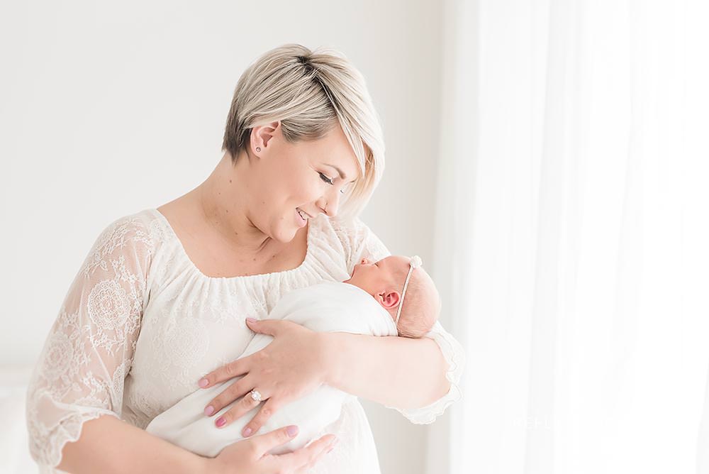 mama holds her baby close and smiles at her in natural light studio
