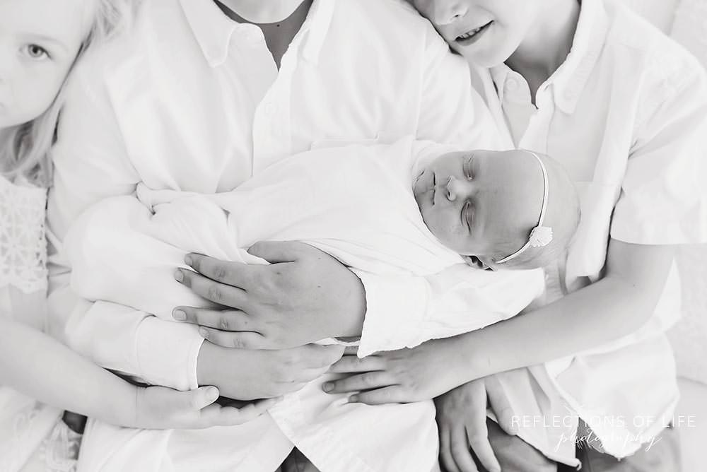 closeup of sleeping newborn as her siblings hold her in black and white