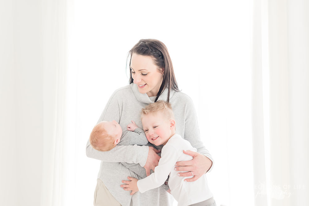 big brother hugs his mama as she holds her newborn in natural light studio