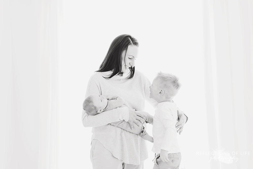 mama smiles at her oldest son as she holds her baby in black and white