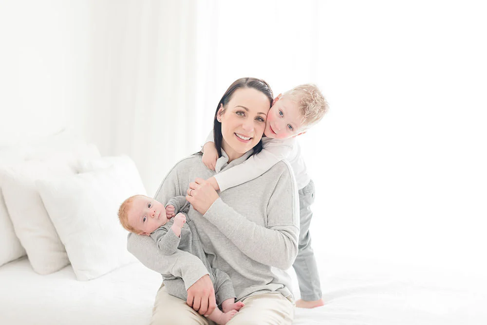 mama holds her two babies as they smile at the camera in natural light studio.jpg