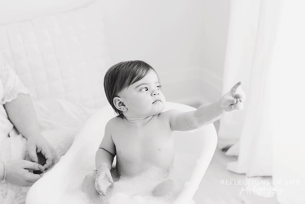 baby looks out the window and points to a bubble in black and white