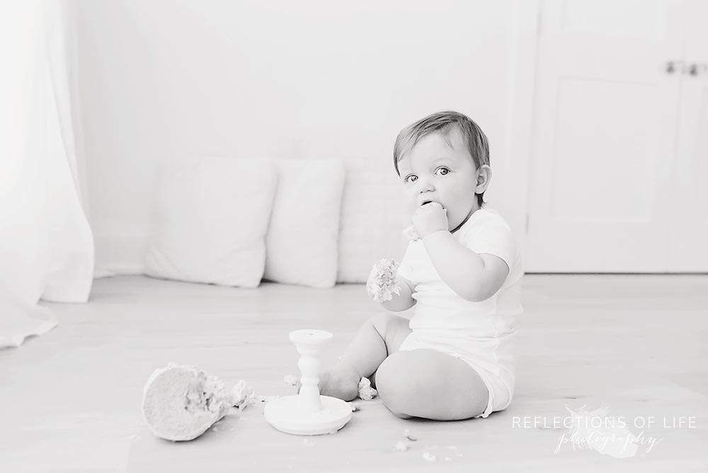 baby eats his cake after it fell on the ground in black and white