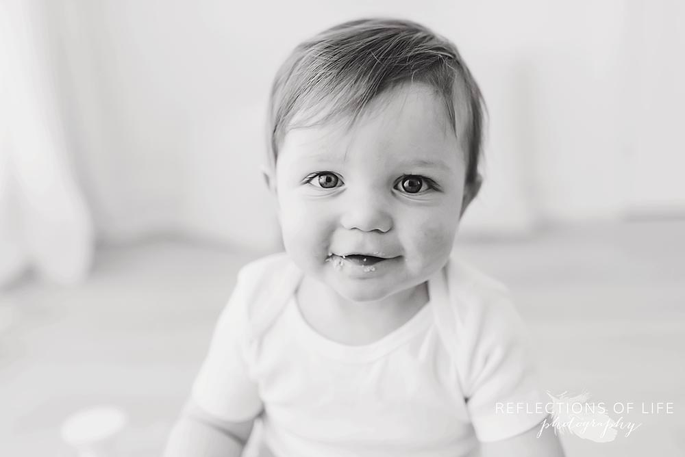 baby smiles at the camera in black and white with cake on his face