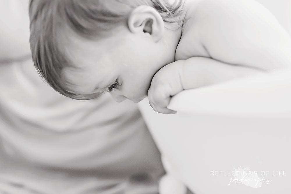 baby looks over the side of the tub in black and white