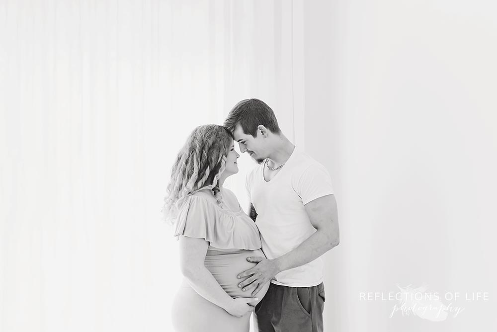 couple looks at each other smiling as he touches her belly in black and white