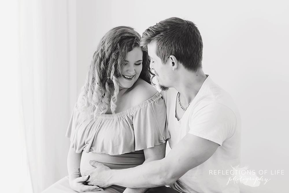 expecting mama smiles and looks down with her husband in black and white