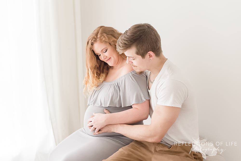 parents look at expecting mamas belly and smile in natural light studio