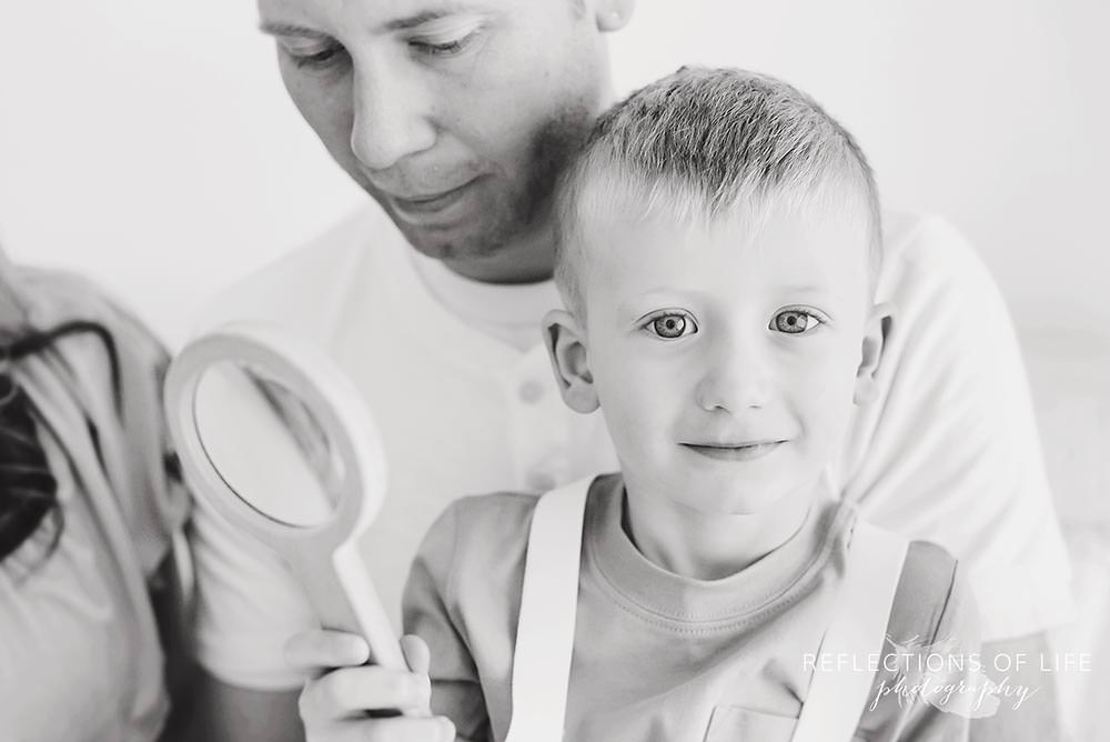 Little boy smiles at the camera with a magnifying glass in his hand niagara child photographer