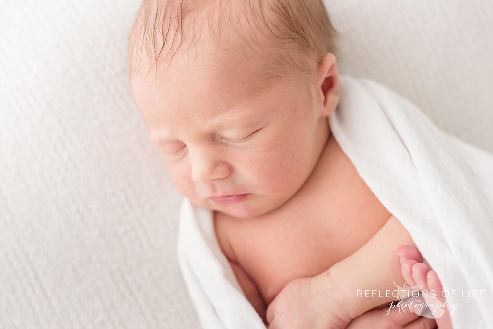 Newborn baby boy wrapped in Little Unicorn bamboo muslin swaddle blanket