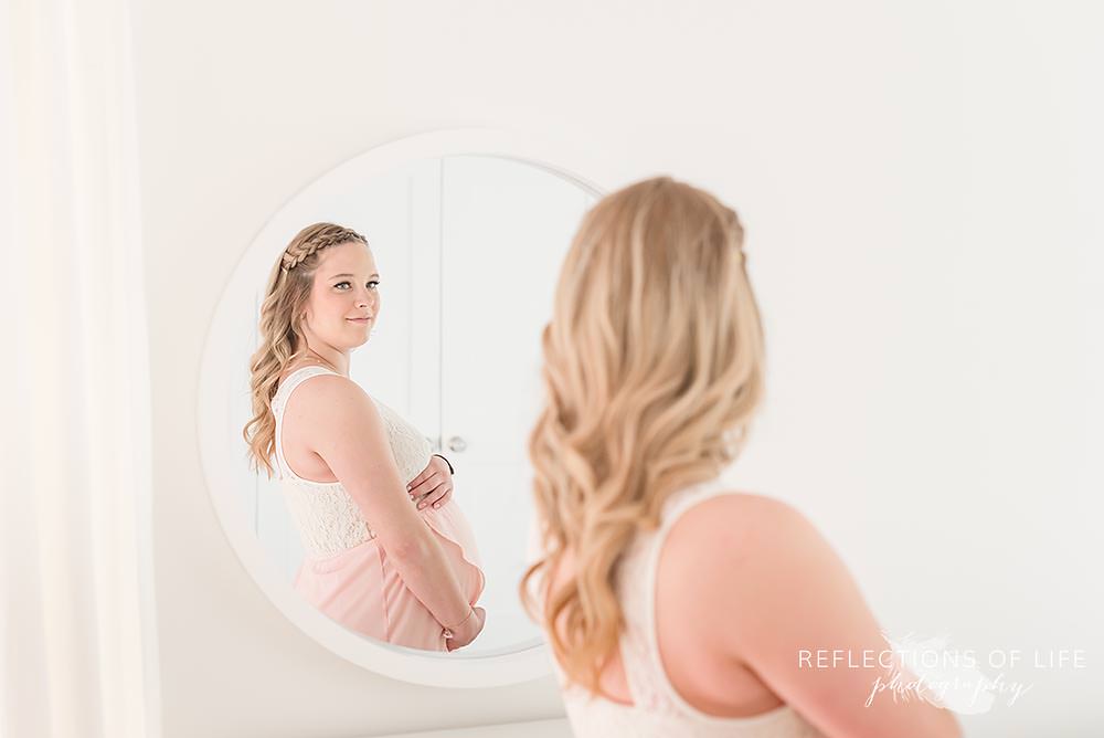 beautiful pregnant mom looks at herself in round mirror