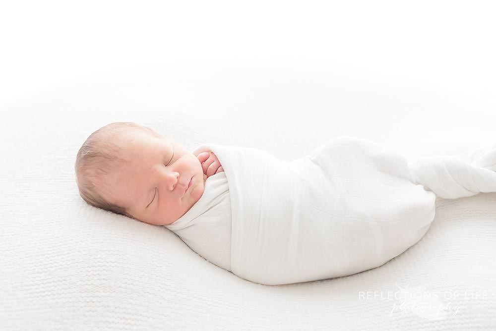 Niagara newborn photographer baby swaddled in white little unicorn blanket