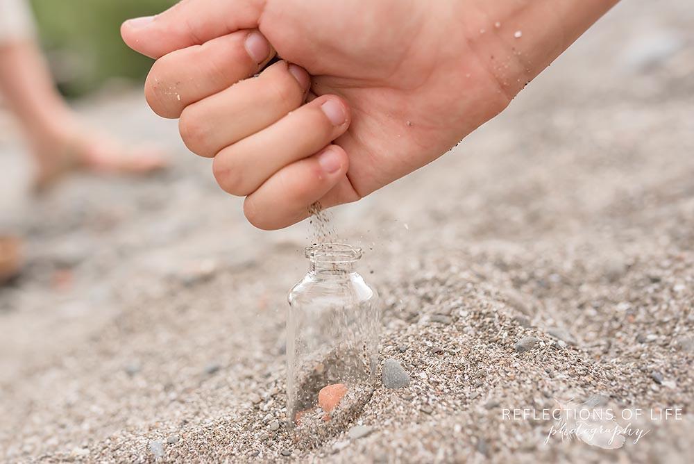 Dropping sand into a small glass jar during a family session in Grimsby Ontario