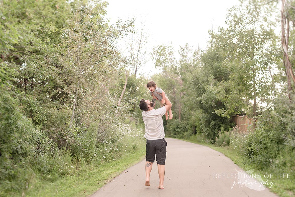 Little boy playing with his Dad on pavement path surrounded in green trees and grass.jpg