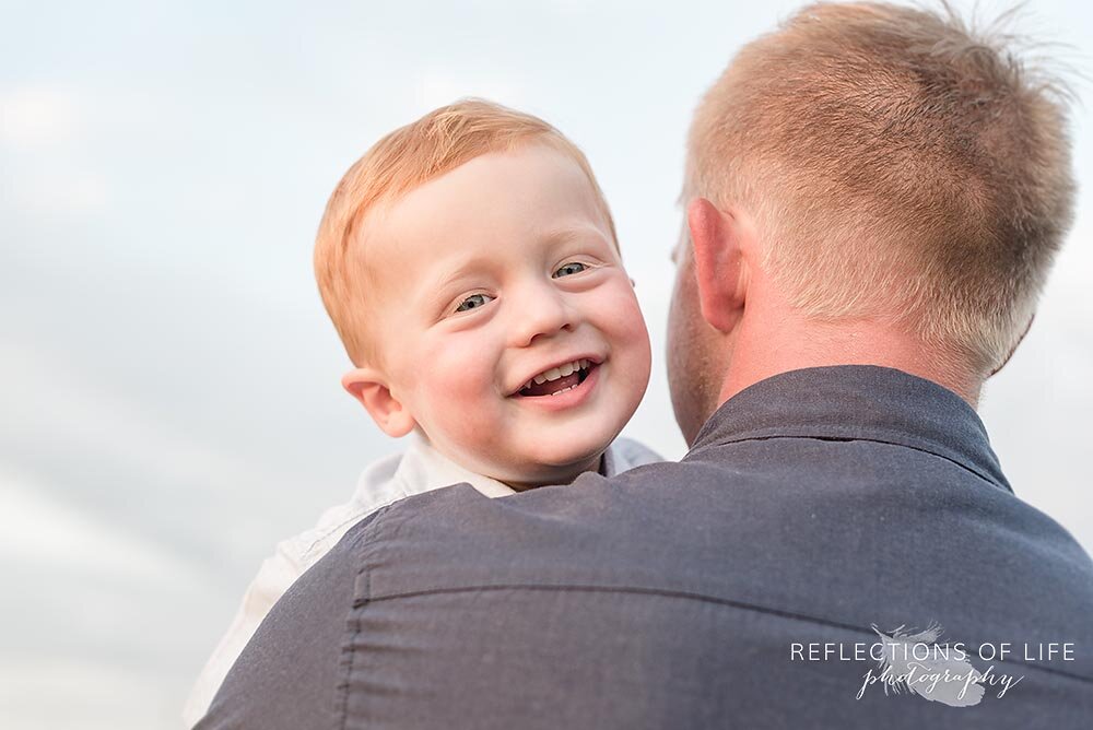 Little boy laughing in their dad's arms