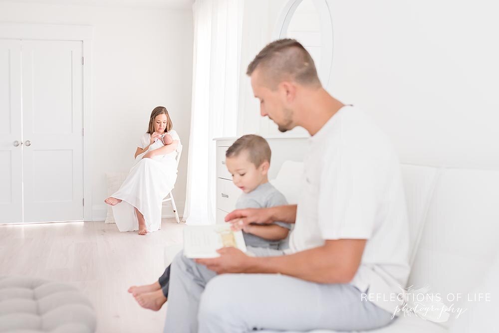 Niagara newborn and family photographer mama feeding baby while dad reads book with sibling.jpg