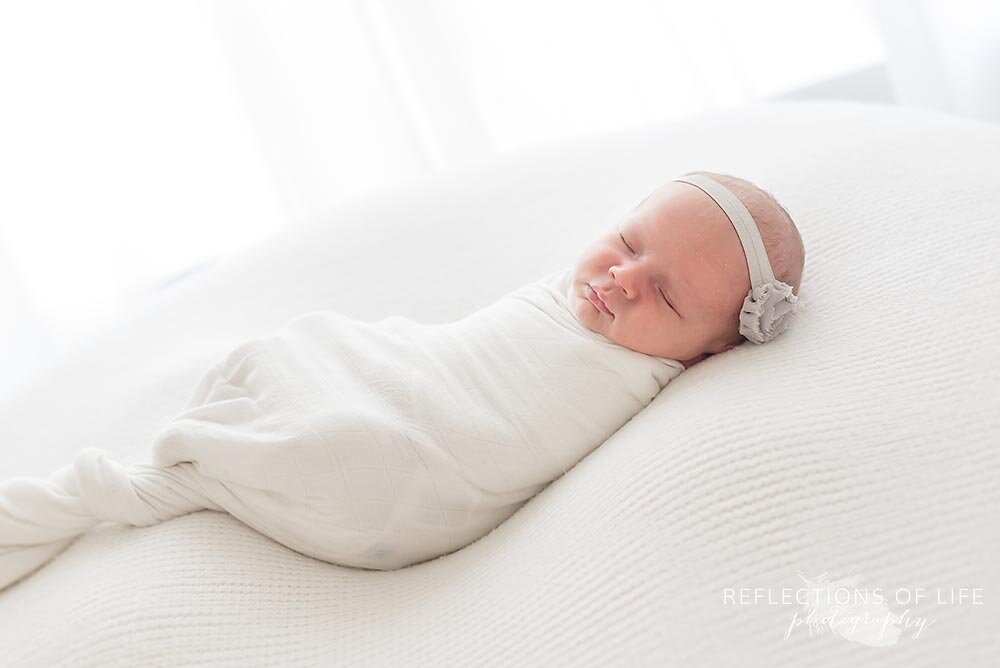 Newborn baby girl laying on white pillow wrapped in white.jpg