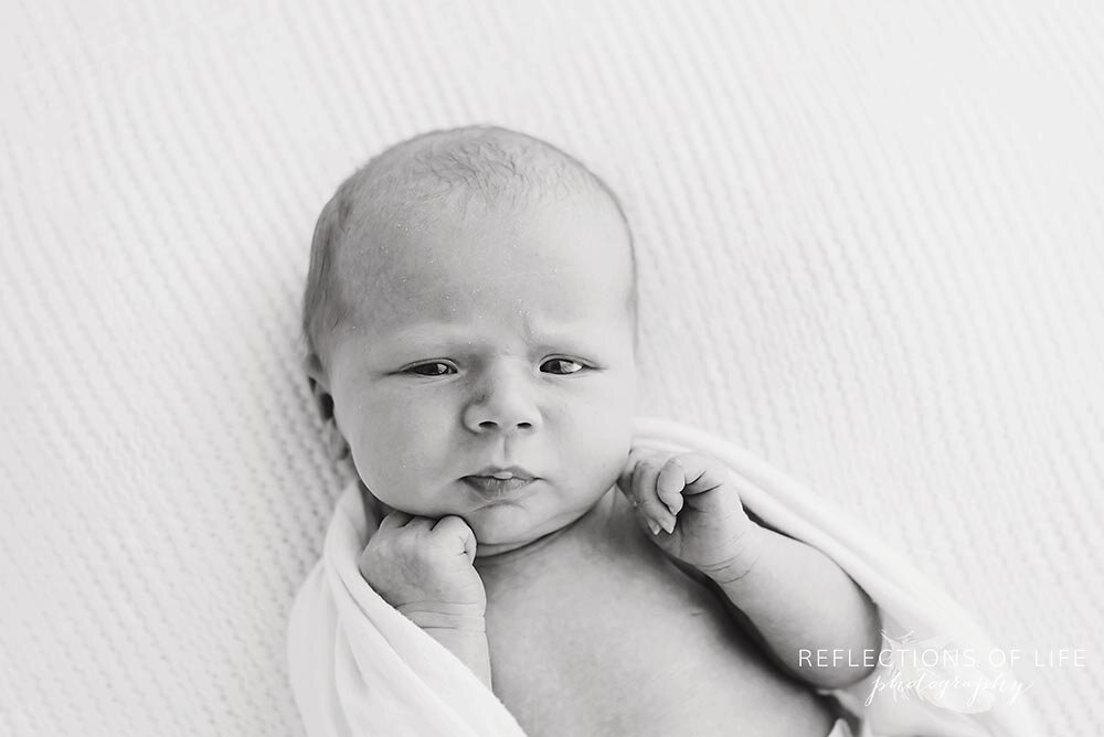 Newborn baby poses with hands under chin in black and white.jpg