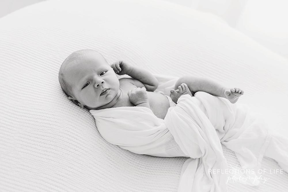 Newborn wrapped in white blanket looking at camera.jpg