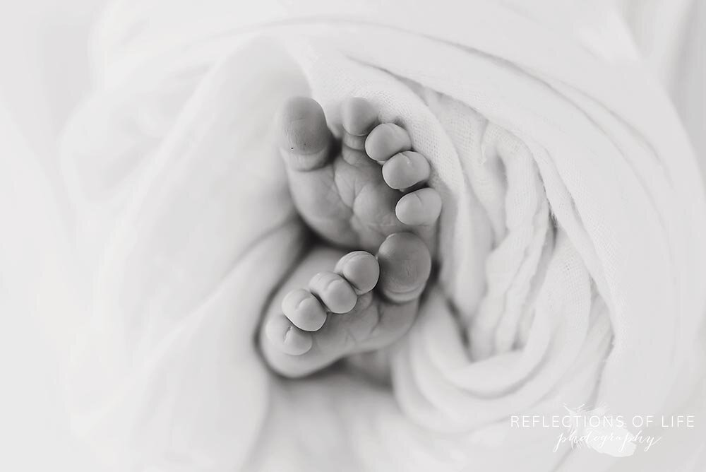 Newborn baby feet wrapped in white swaddle blanket