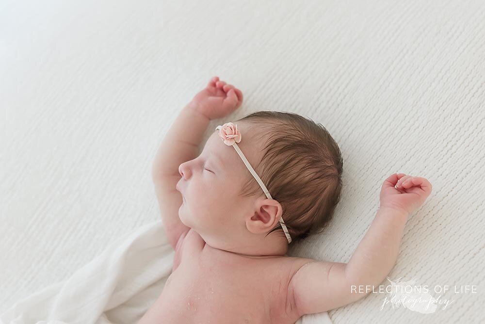 Newborn baby laying down with hands in the air