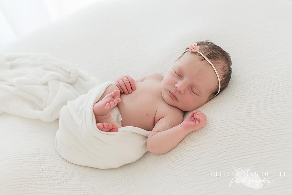 Newborn baby girl laying on her back white natural photography