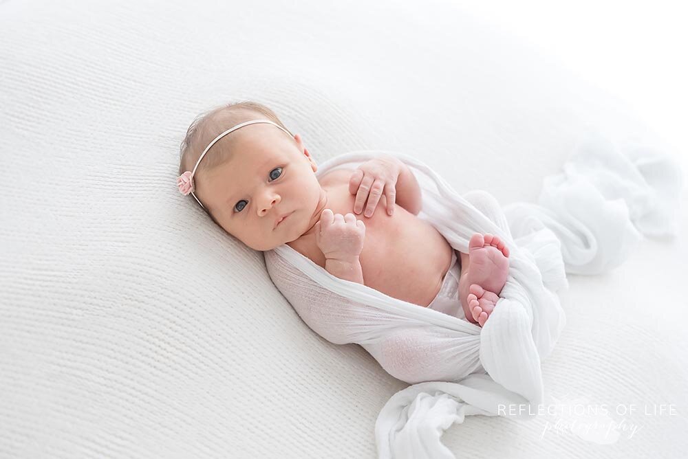 Newborn baby girl wrapped in swaddle blacket looking into camera Reflections of Life Photography