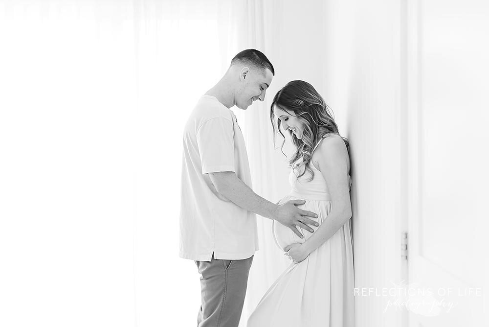 Mom and Dad look down at pregnant belly in Grimsby Ontario photo studio