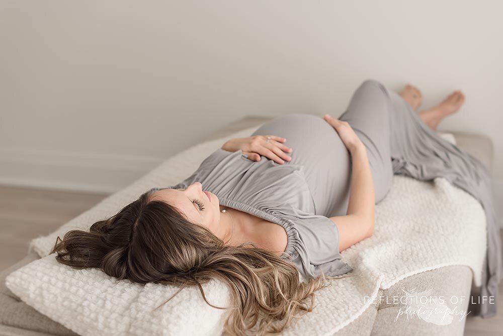 Maternity photo of mom laying on her back in pretty gray casual dress Niagara Ontario photo studio