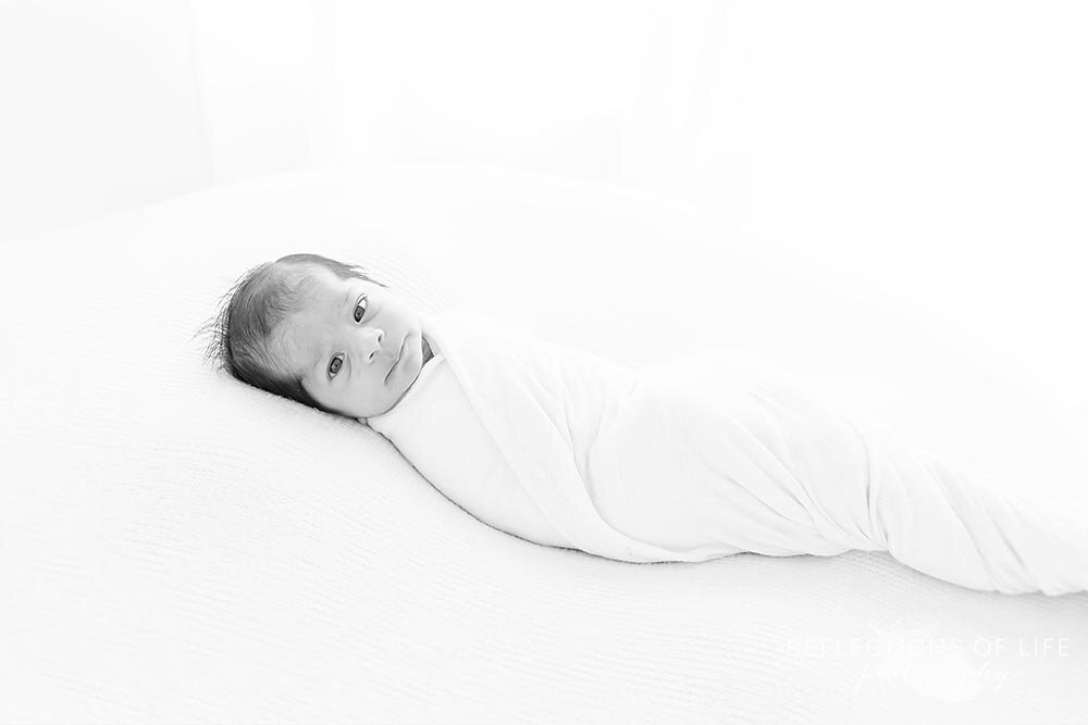 Little baby boy swaddled in backlight in white on a while backdrop