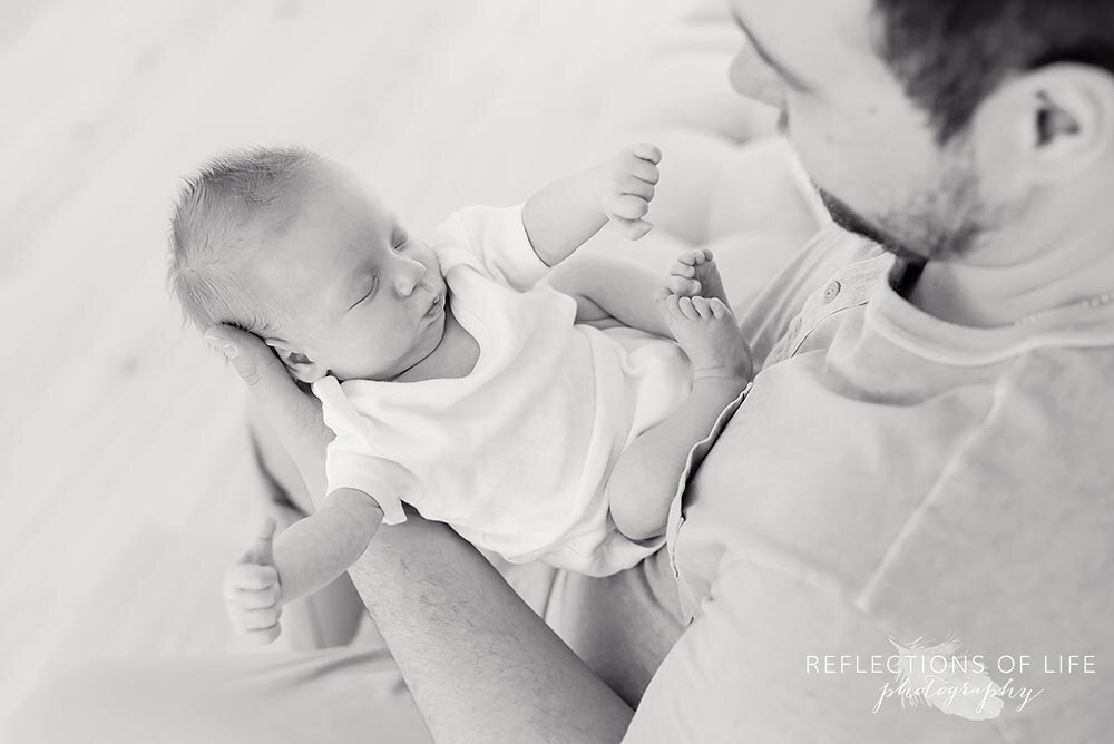 Baby boy in white onesie stretching in his daddys arms Niagara Falls Ontario Canada