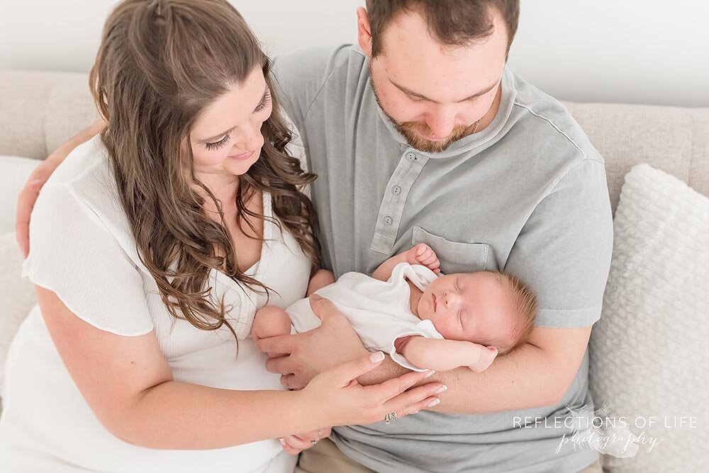 New young family poses on couch with newborn baby in their arms Niagara Ontario Canada