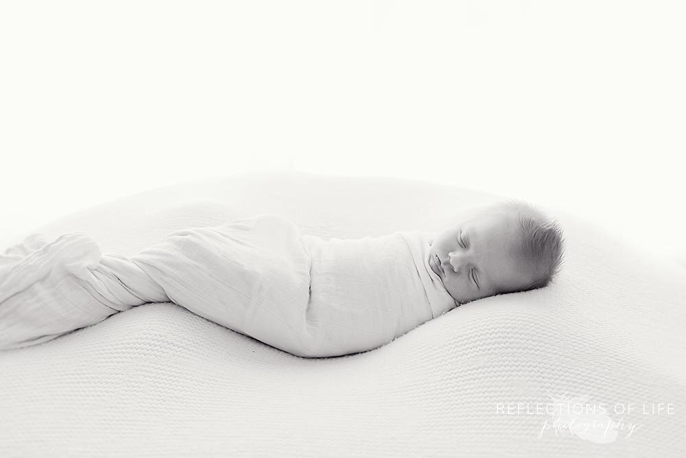 Little newly born baby boy swaddled in little unicorn white swaddle blanket