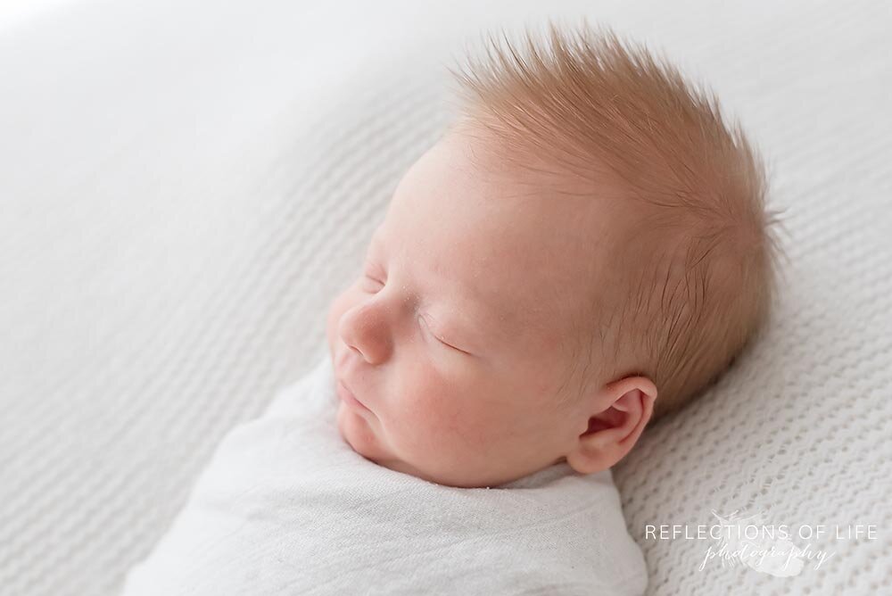 New baby redhead in white swaddle blanket Grimsby Ontario natural light photo studio
