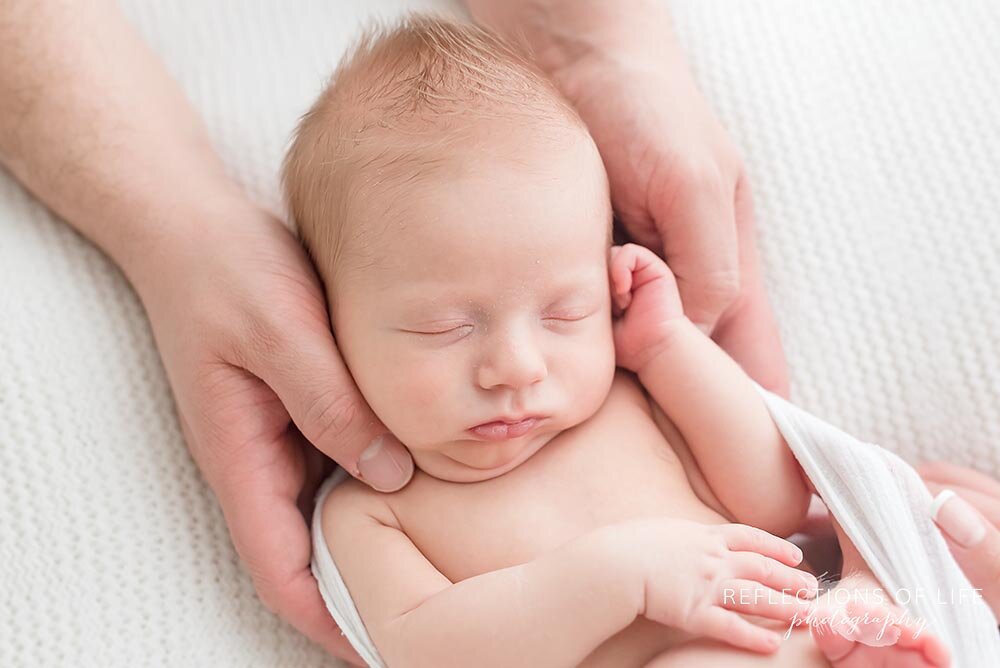 Adorable close up of newborn baby boy with his parents hands on him Niagara Ontario Photo Studio