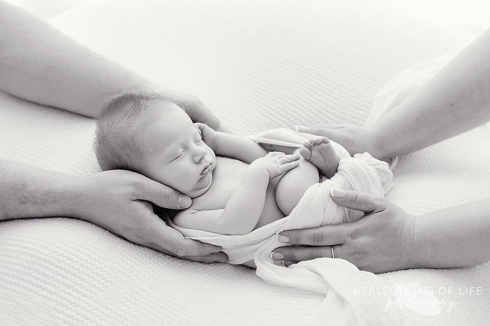 Newborn baby boy with his parents hands on him Natural newborn photography Niagara